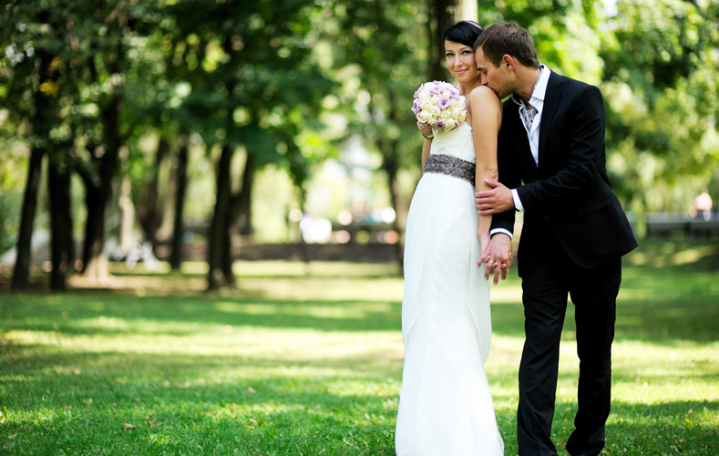 Happy bride and groom on their wedding day holding bouquet of roses and holding her hand